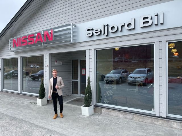 Bilde av en bil ogtre personer som ser på biler hos en bilforhandler